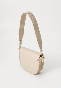 Béžová crossbody taška s hladkým koženým povrchem, kulatým tvarem, překlápěcí klopou a texturovaným ramenním popruhem s reliéfním nápisem.