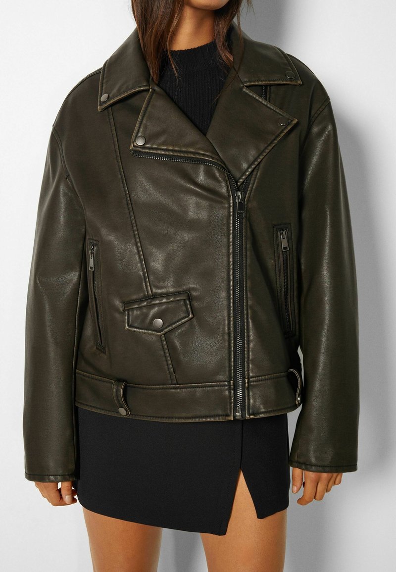 Mörkgrön läderbikerjacka med oversized passform, dragkedja fram och sidfickor. Har en spetsig krage och tryckknappdetaljer.