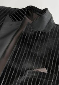 Black velvet blazer featuring vertical stripes of sequins and a satin pocket square. Smooth texture with a shawl collar design.