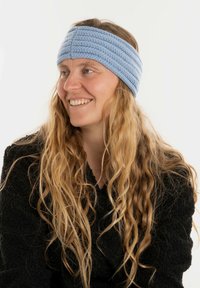 Fascia blu all'uncinetto con un design a coste e texture, indossata da una persona con lunghi capelli mossi, su uno sfondo neutro.