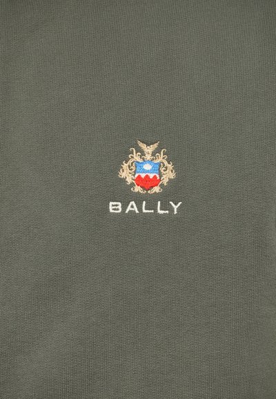 Tela verde con el logotipo bordado de Bally, que presenta un escudo azul, rojo y beige sobre el texto blanco de Bally.