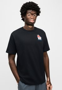 Μαύρο βαμβακερό t-shirt με πολύχρωμο γραφικό λογότυπο στο αριστερό στήθος. Κοντά μανίκια, στρογγυλή λαιμόκοψη και άνετη εφαρμογή.