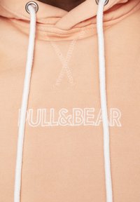 Felpa pesco con logo "PULL&BEAR" ricamato in bianco, con lacci bianchi e occhielli metallici. Tessuto morbido e strutturato con dettagli di cucitura.