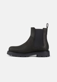 Botín Chelsea de cuero negro con paneles laterales elásticos, tirador y suela de goma texturizada para mayor agarre. Diseño elegante y acabado discreto.