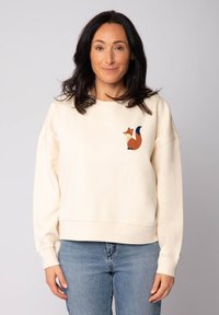 Crèmewitte sweatshirt met een ontspannen pasvorm, met een afbeelding van een vos in oranje en blauwe accenten op de linkerborst. Zachte stoftextuur.