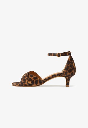 Bruine en zwarte suède sandaal met luipaardprint, lage kittenhak en enkelbandje met goudkleurige gesp, getoond in zijprofiel.