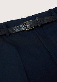 Zbliżenie na granatowe spodnie z teksturowanym czarnym skórzanym paskiem przewleczonym przez szlufki i zapiętym złotą klamrą.