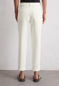 Pantalones de mezclilla blancos con corte recto, con dos bolsillos traseros de parche y puños enrollados. Textura suave y diseño minimalista.