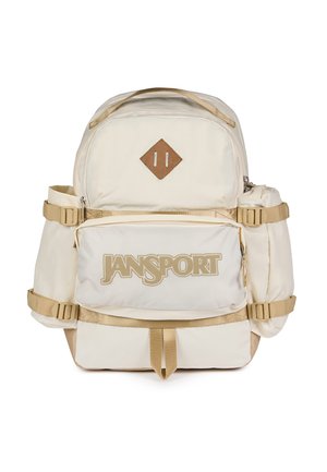 Beige Jansport-reppu, jossa edessä vetoketjutasku, sivutaskut, säädettävät olkahihnat ja ruskea timantinmuotoinen merkki yläosassa edessä.