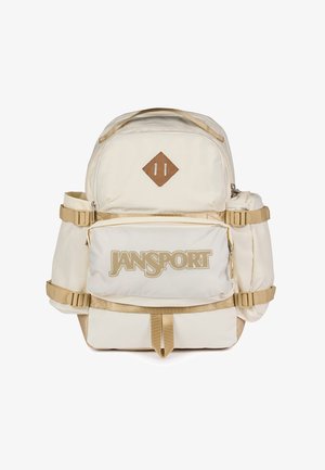 Beżowy plecak Jansport z przednią kieszenią na zamek, bocznymi przegródkami, regulowanymi paskami i brązową łatką w kształcie diamentu na górze z przodu.