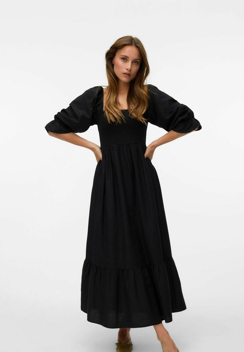 Robe maxi noire avec un buste froncé, des manches bouffantes et un ourlet volanté. Fabriquée en tissu léger, offrant une silhouette fluide.
