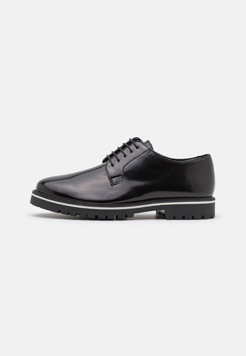 Chaussure de ville en cuir noir poli à lacets avec semelle épaisse en caoutchouc et détail d'une bande blanche sur fond clair uni.