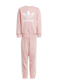 Svetloružová mikina a zodpovedajúce jogger nohavice vyrobené z mäkkej tkaniny. Obsahuje bielu Adidas logo a biele bočné pásiky na nohaviciach.