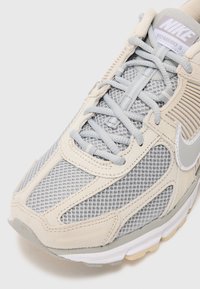Nike Vomero 5 tenisice u svijetlo sivoj i bež boji, sa mrežnim i antilop materijalima, istaknutim vezanjem i prepoznatljivim logotipom na jeziku.