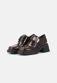 Burgundy patent leather shoes with a block heel, featuring a large metallic buckle detail and stitched accents on the toe area.