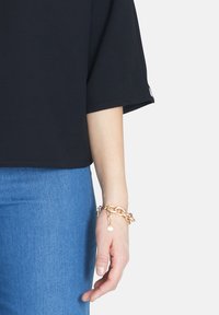 Sort kortærmet top med en løs pasform, parret med blå denim. Accessoriseret med et chunky guldkædearmbånd på håndleddet.