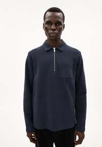 Navy pullover with long sleeves, zip collar, and front patch pocket; features soft fabric and a small logo in the corner.