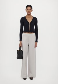 Svart, ribbete strikket cropped cardigan med dyp V-hals, kombinert med lysegrå, vide bukser og en liten svart håndvask.