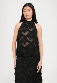 Černý halter top s vrstvenými, třásněmi v chevronovém vzoru, vyrobený z lehké, průsvitné tkaniny s hladkým límcem.