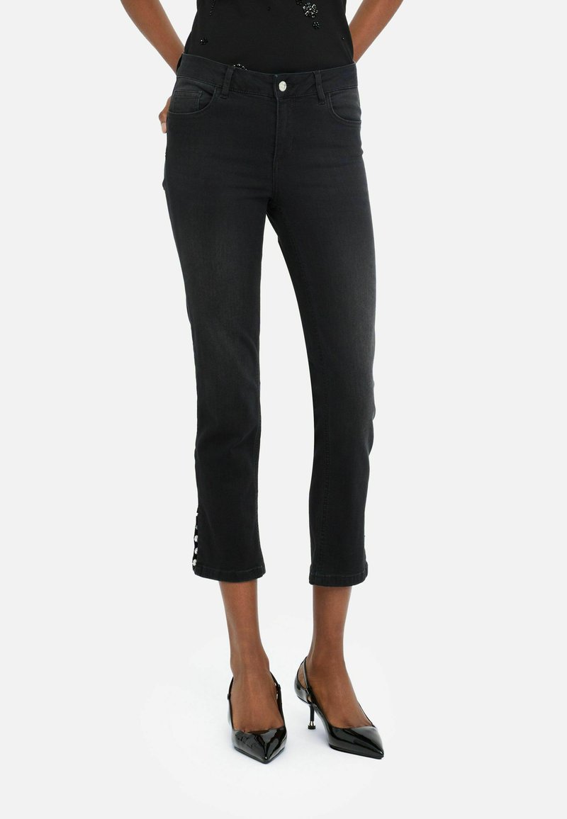 Jean noir cropped avec une coupe slim, des détails au niveau de l'ourlet et un design traditionnel à cinq poches. Associé à des chaussures à talons hauts noires.