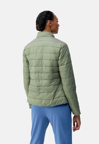 Lichtgroene, gequiltte jas met een opstaande kraag, met een slim fit silhouet en een textuurpatroon. Geddragen over blauwe broek.