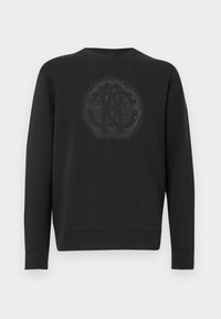 Czarna bluza z miękkiego materiału, z teksturowanym okrągłym logo pośrodku, otoczonym dekoracyjnymi akcentami. Długie rękawy.