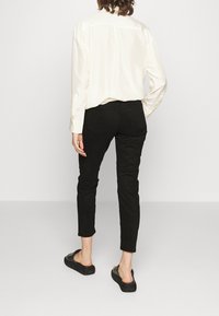 Zwarte broek met een slim fit, elastische tailleband en twee achterzakken. Gecombineerd met een lichtgekleurde, lange mouwen shirt.