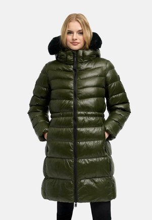 Femme portant un long manteau matelassé vert olive brillant avec une capuche bordée de fourrure noire, mains dans les poches, debout sur un fond clair uni.