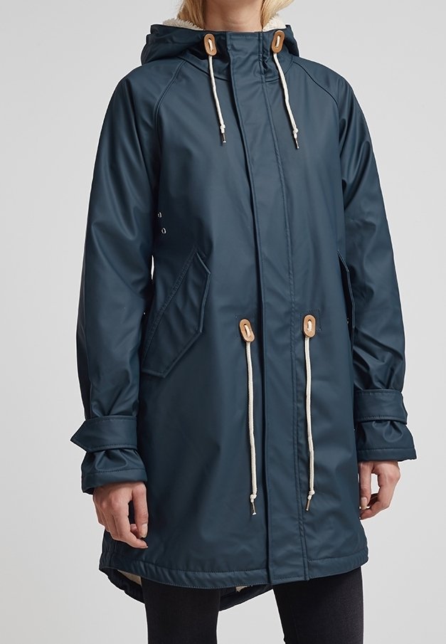 Imperméable à capuche bleu marine avec cordons blancs et boutons en bois, poches à rabat et sangles de poignets ajustables porté par une personne.
