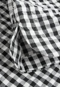 Crno-bijela gingham tkanina s uzorkom mreže, izrađena od teksturirane, tkane pamučne tkanine. Rubovi su obrubljeni vidljivim šavovima.
