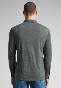 Grijs overhemd met lange mouwen, gemaakt van een textuurstof, met een kraag en knoopsluitingen bij de mouwen, gedragen met blauwe spijkerbroek.