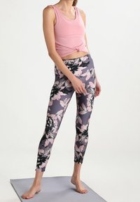 Top corto de color rosa claro con un detalle anudado, combinado con leggings ajustados que presentan un estampado floral en tonos de rosa y negro sobre un fondo gris.
