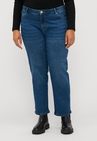 Jeans in denim di colore blu scuro con una vestibilità dritta, design a cinque tasche, chiusura con bottone e una leggera scoloritura, abbinati a stivaletti neri alla caviglia.