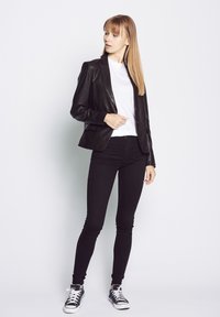 Schwarze Lederblazer mit tailliertem Schnitt über einem weißen T-Shirt, kombiniert mit schwarzen Skinny-Jeans und schwarz-weißen Sneakers.