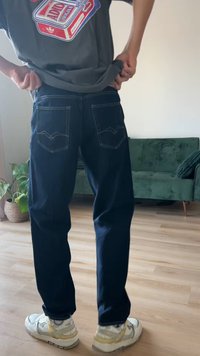 Sötétkék farmernadrág látható varrással, két hátsó zseb zigzag mintával, fehér tornacipővel viselve hétköznapi környezetben.