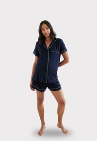 Granatowy zestaw piżamowy z krótkim rękawem z białym wykończeniem, składający się z koszuli zapinanej na guziki z kieszonką oraz dopasowanych szortów. Miękki materiał, luźny krój.