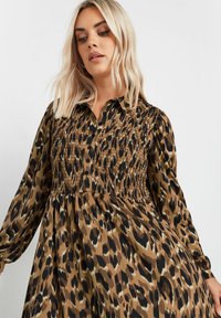 Sukienka w panterkę w odcieniach brązu i czerni, z marszczonym gorsetem, długimi rękawami i zapięciem na guziki. Miękka tkanina o płynącym kroju.