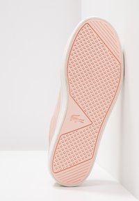 Semelle de basket rose clair avec motif texturé, accents blancs et un logo. Elle présente une finition lisse et un dessin géométrique de la bande de roulement.