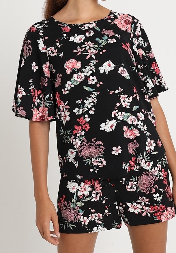 Conjunto floral negro que incluye una camiseta de manga corta y pantalones cortos. El diseño presenta flores rosas y blancas con acentos verdes. Tejido suave y corte relajado.