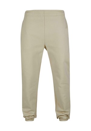 Jogging en coton beige avec une coupe fuselée, taille élastique et chevilles côtelées. Caractéristiques d'une texture lisse et de détails de couture subtils.