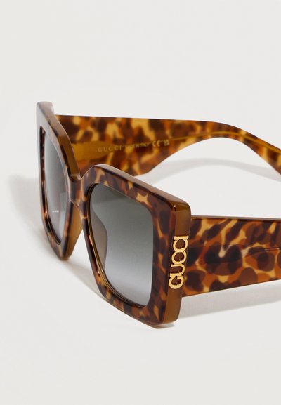 Τετράγωνα γυαλιά ηλίου με μοτίβο χελώνας, σκοτεινούς φακούς με βαθμιαία απόχρωση και χρυσό λογότυπο Gucci στο πλάι του βραχίονα.