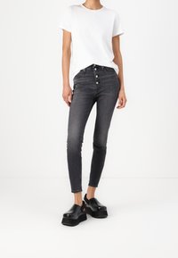 Jeans o wysokim stanie, dopasowane, w ciemnoszarym denimu, z zapięciem na guziki, bocznymi kieszeniami i przetarciami. W połączeniu z białym t-shirtem i czarnymi klapkami na platformie.