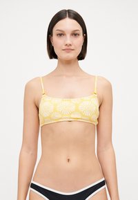 Žltý bikiny top s tenkými ramienkami, zdobený bielymi kvetinovými vzormi. Navrhnutý v obdĺžnikovom tvare s hladkým povrchom.