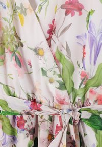 Gros plan d’un tissu avec un imprimé floral coloré en vert, rouge, violet et rose, noué en nœud à la taille sur fond clair.