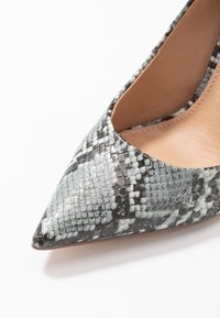 Chaussure à talon aigu en matériau synthétique à motif reptilien gris et noir. Texture lisse avec une doublure intérieure beige.