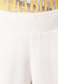 Tessuto bianco con una texture e un motivo stropicciato. La vita è arricciata per offrire elasticità, con un design colorato in alto.