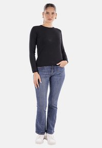 Top a maniche lunghe nera, design aderente, abbinato a jeans azzurri e sneakers bianche. Estetica semplice e versatile, texture liscia.