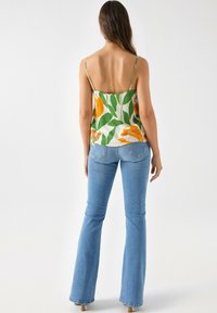 Camiseta sin mangas floral con patrones verdes y naranjas; tela ligera; tirantes finos. Combinada con unos pantalones vaqueros de campana ajustados de color azul claro.