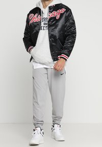 Sort satin bomberjakke med rød og hvid "Chicago" skrift, grå hættetrøje under, grå træningsbukser og hvide sneakers.