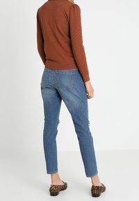 Pull marron texturé, jean en denim bleu slim, et ballerines à imprimé léopard. La tenue présente une silhouette ajustée et un style décontracté.
